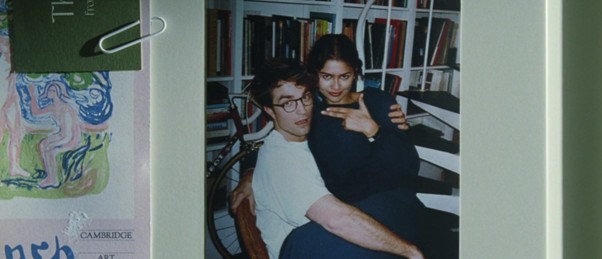 Une photo d'un homme assis avec des lunettes, tenant une femme qui pose, avec des étagères de livres en arrière-plan.